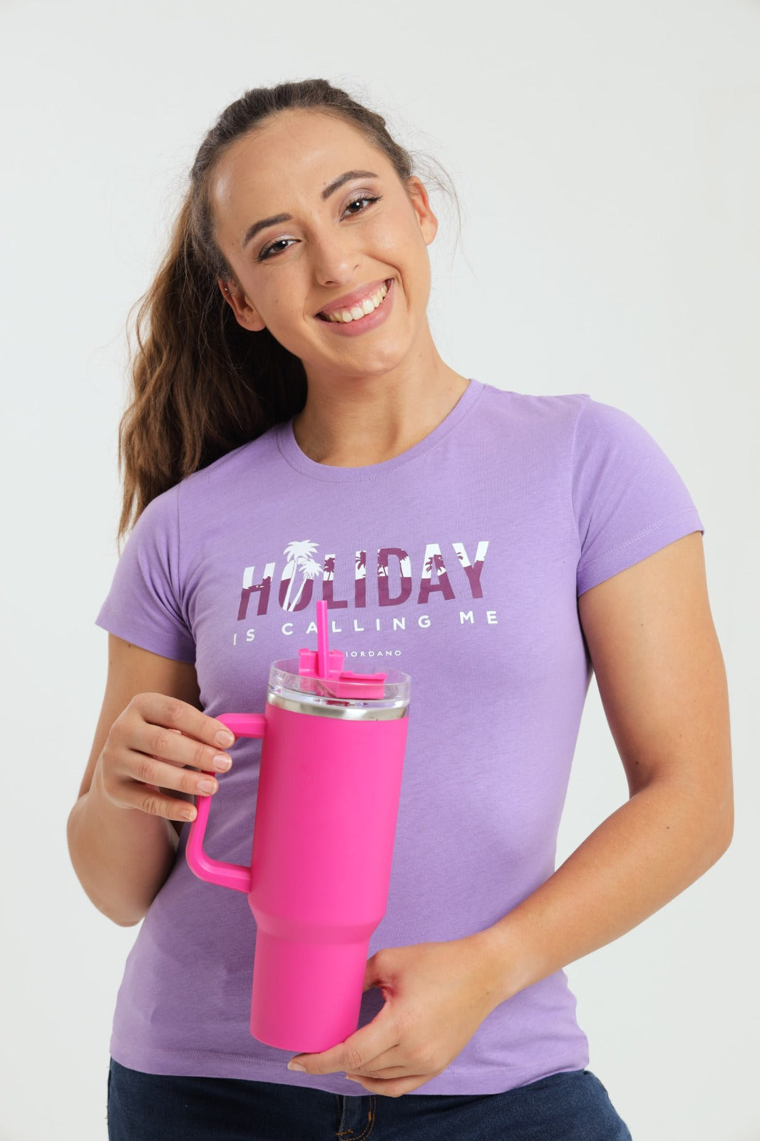 Woman wearing a purple t-shirt with text holding a pink tumbler against a white background