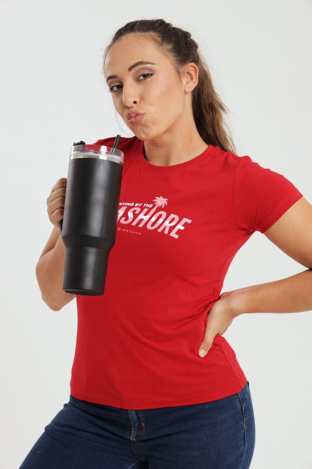 Woman wearing a red t-shirt with text, holding a black tumbler against a white background