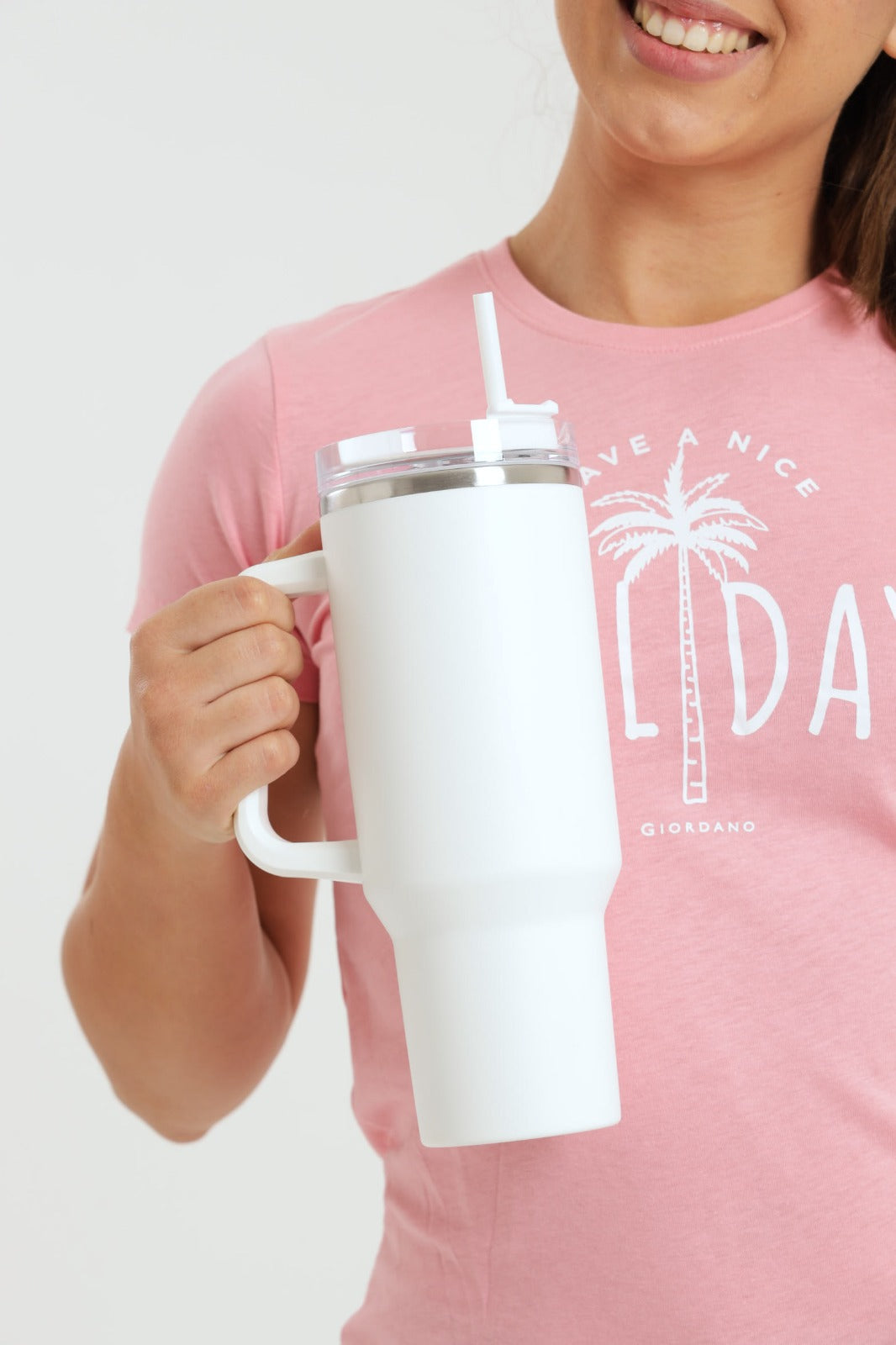 Person holding a white tumbler with a straw, wearing a pink shirt with a palm tree design.