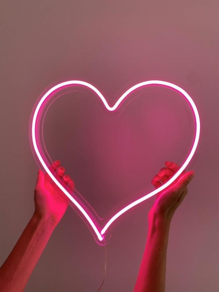 Neon heart shape held by hands against a dark background