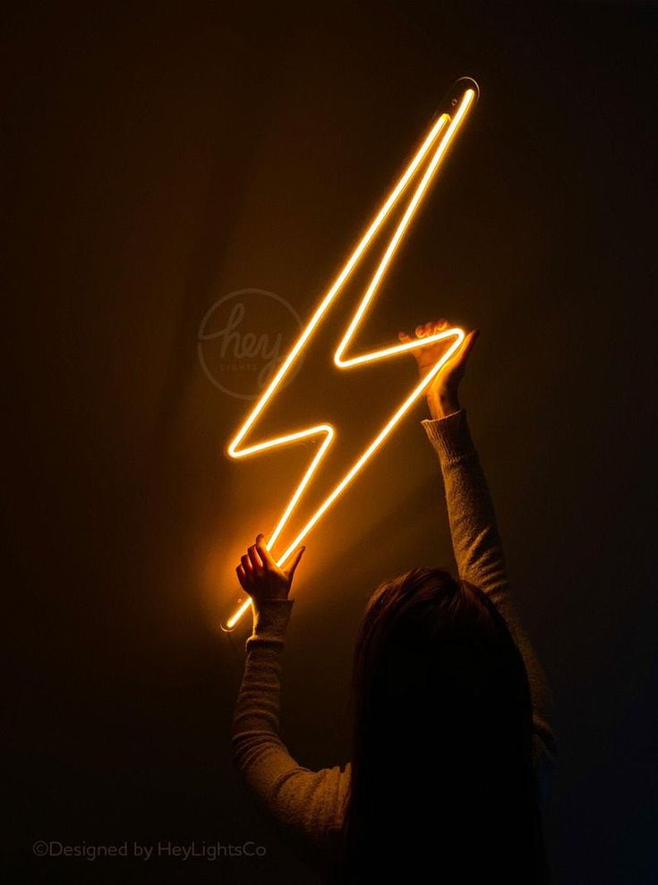 Person holding a neon lightning bolt shape against a dark background